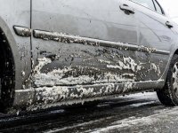 Documentary photograph of realistic winter road salt and grime accumulated on the lower panel of an everyday commuter car